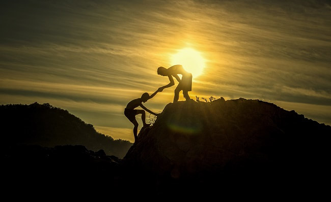 Person helping another person reach the top of a mountain