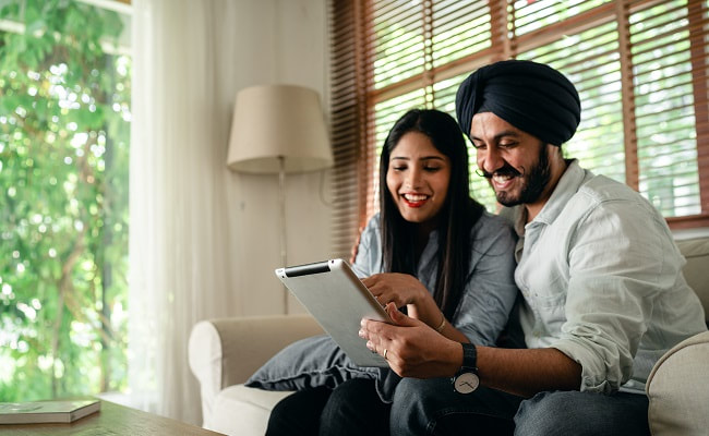 Indian couple sitting on a sofa using a tablet device.