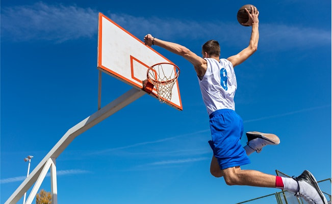 Man jumping to slam dunk basketball into hoop