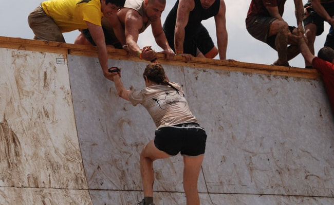 People helping a young woman get over a wall